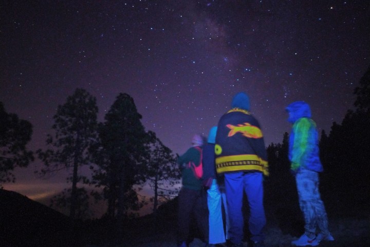 a group of people standing in a dark sky stargazing