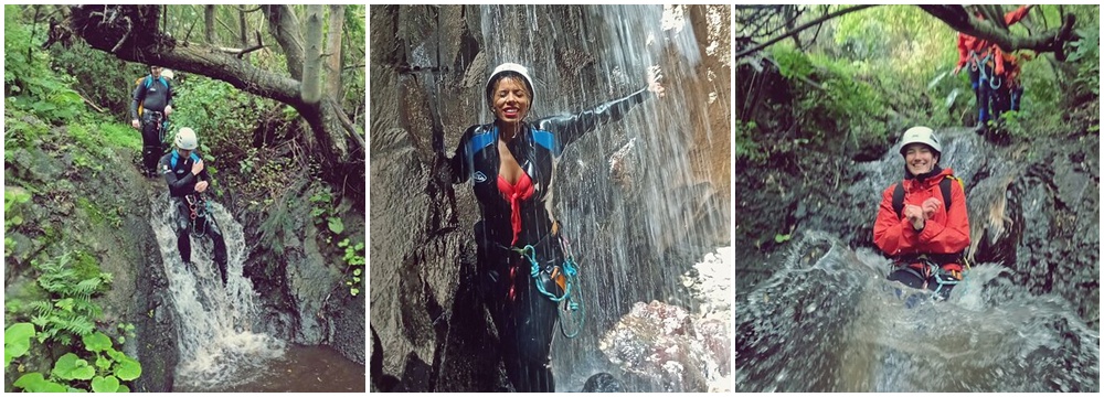 Three people canyoning; navigating rocks and waterfalls in helmets and wetsuits.