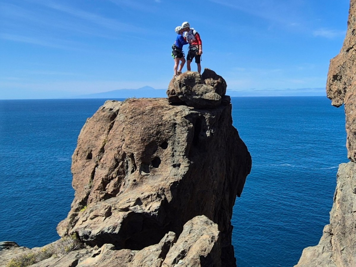 Climbers on rocky cliff overlooking ocean, sunny day, clear blue sky