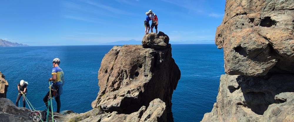 Climbers on rocky cliff overlooking ocean, sunny day, clear blue sky