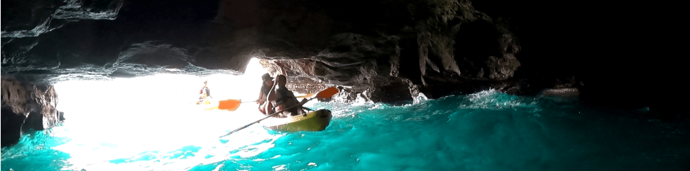 Two people kayaking in a bright cave with turquoise water.