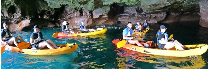 Group of people kayaking in a cave with clear water and rocky walls.