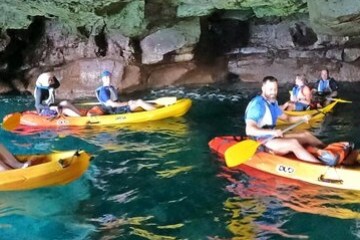 Group of people kayaking in a cave with clear water and rocky walls.