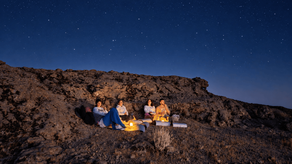 Four people sitting on a rocky hill under a starry night sky.