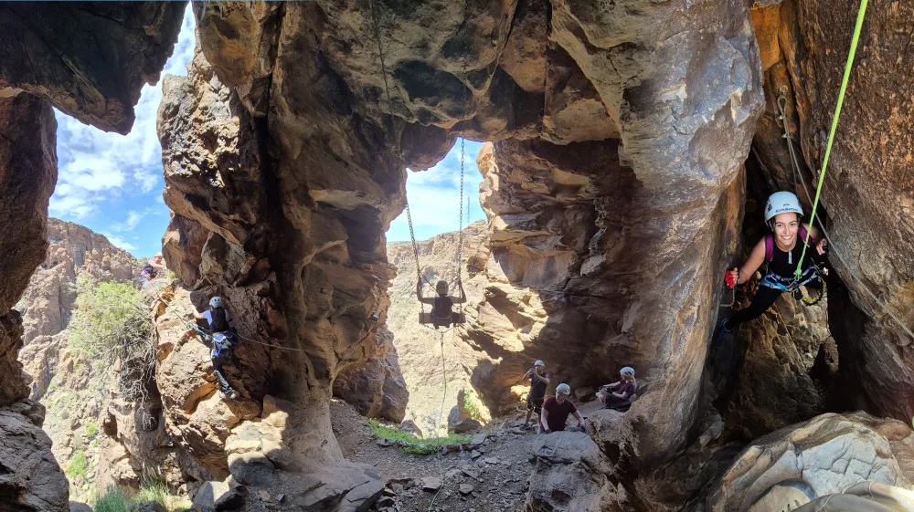 People rock climbing in a canyon with a rope swing in the center.