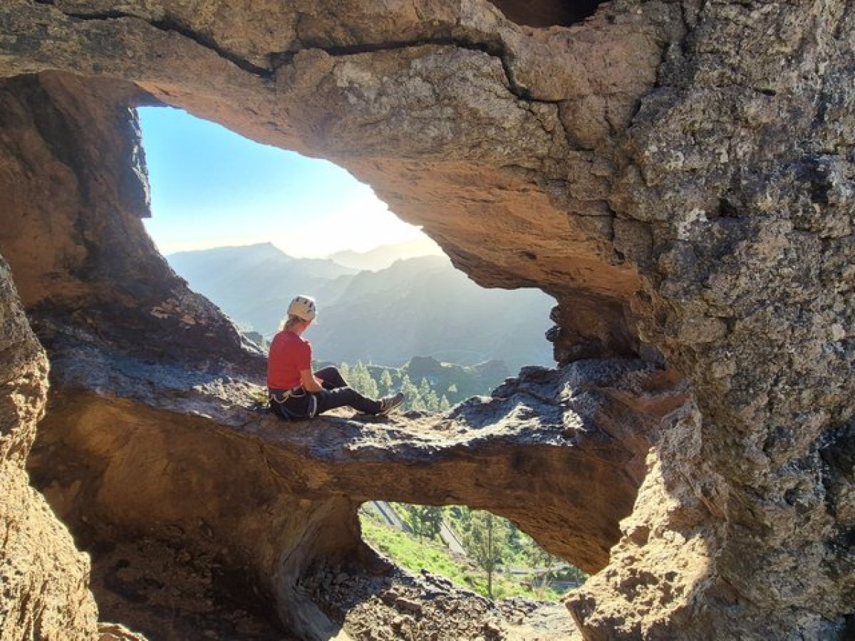 Person sitting in a rock formation, overlooking mountains and valleys.