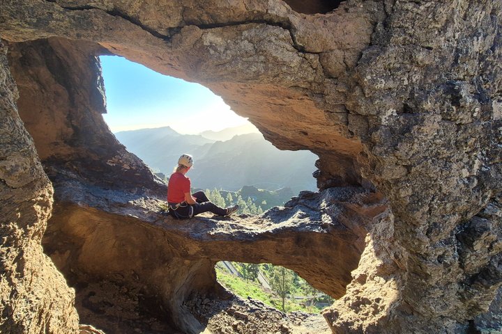 Person sitting in a rock formation, overlooking mountains and valleys.
