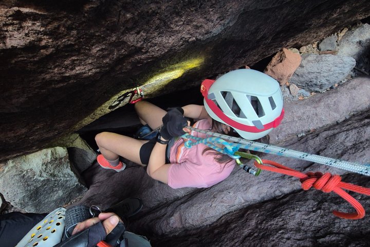 Person in helmet and harness climbing through a narrow rock crevice.
