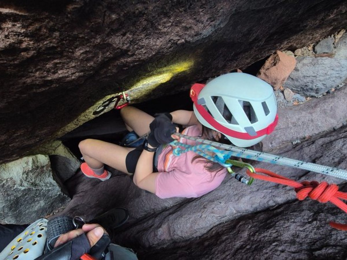 Person in helmet and harness climbing through a narrow rock crevice.