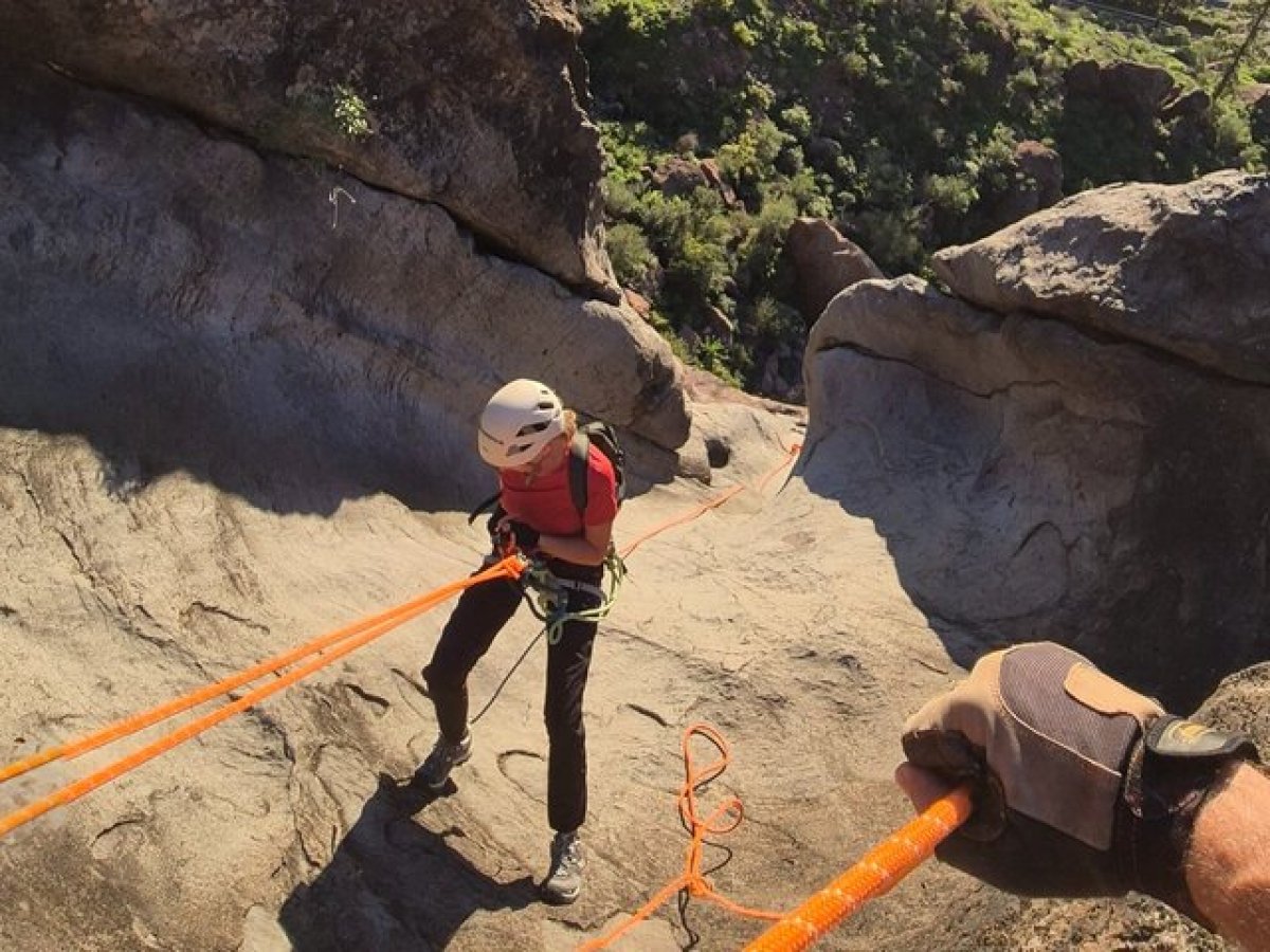 Person wearing helmet rappelling down rocky slope using orange ropes.